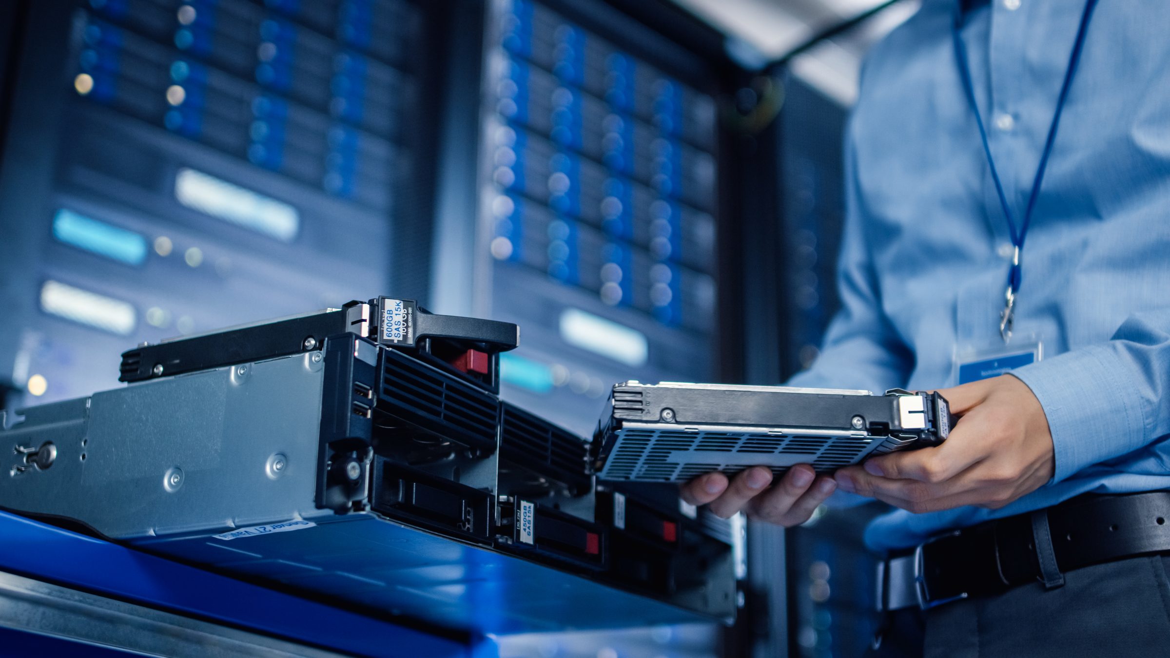 Engineer holding a hard drive beside a server rack in a data centre