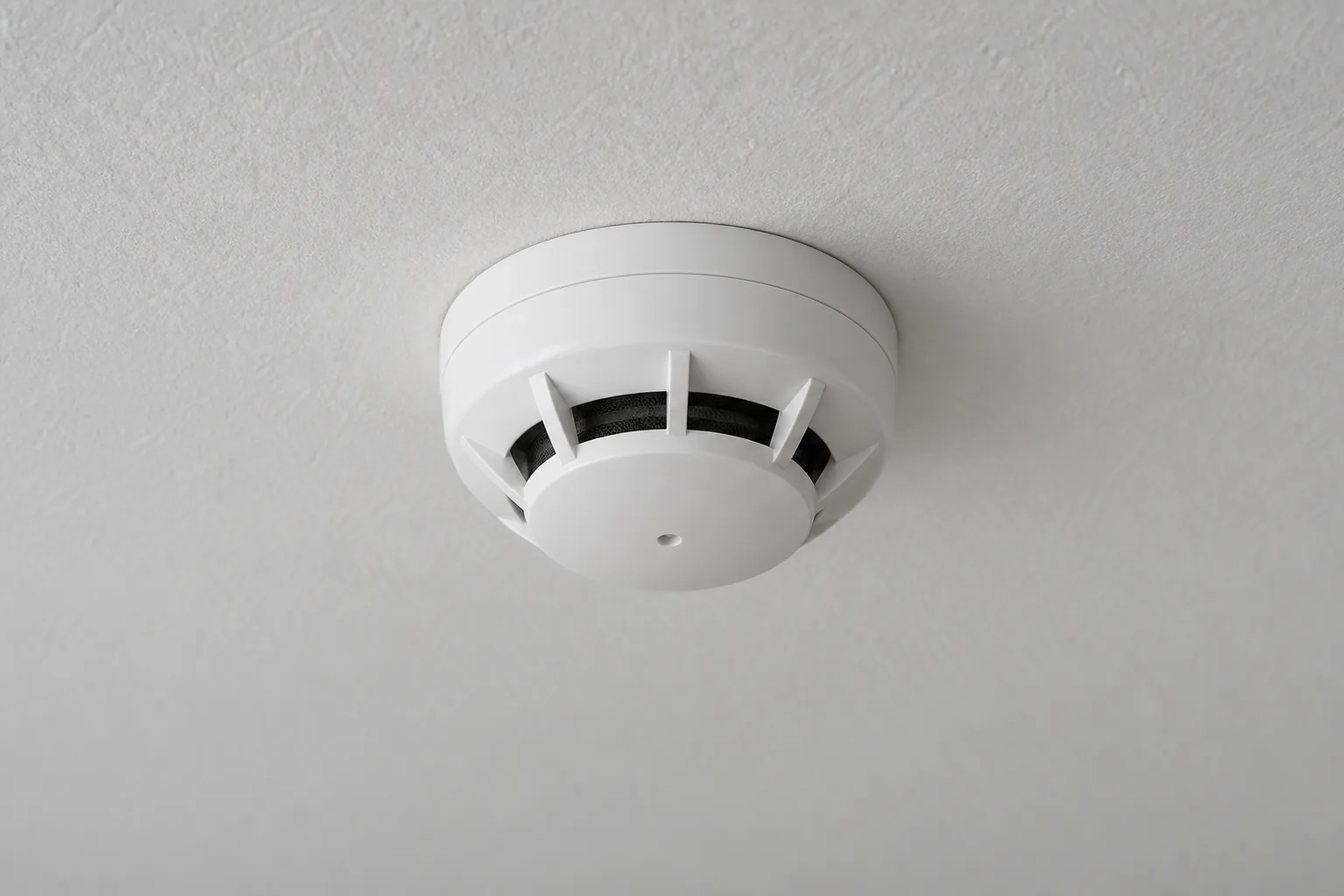 Close view of a white vented fire detector on a plain ceiling.
