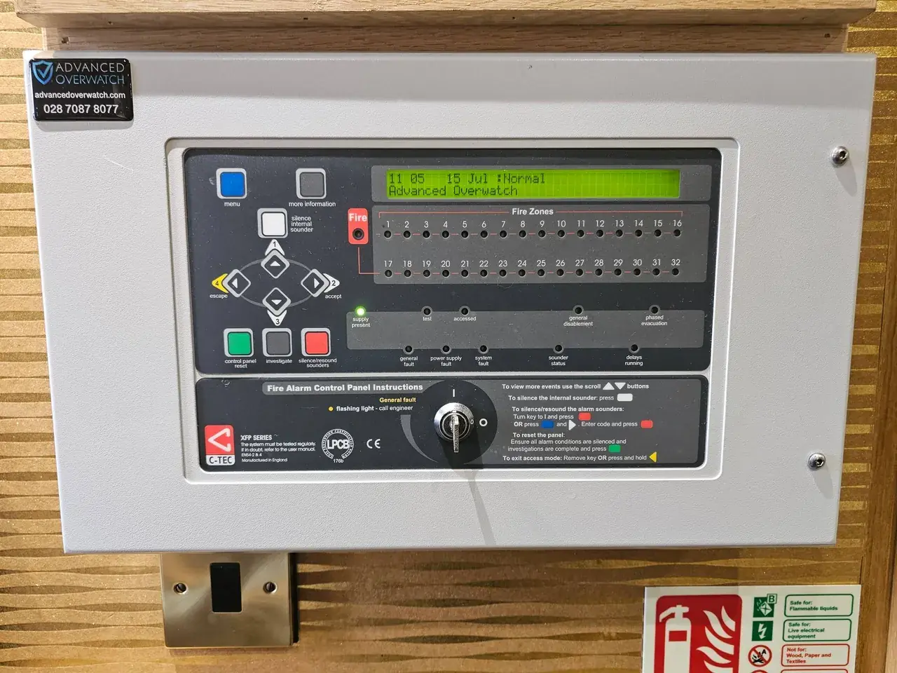 C-TEC XFP fire alarm control panel showing a normal status display, with Advanced Overwatch contact details on the enclosure